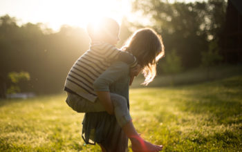 auf einer grünen Wiese: ein Mädchen trägt einen kleineren Jungen auf ihrem Rücken