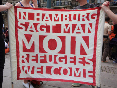 Banner auf einer Demonstration mit der Aufschrift "In Hamburg sagt man Moin Refugees Welcome"