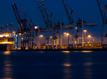 Kräne im Hamburger Hafen bei Nacht, davor ein Containerschiff