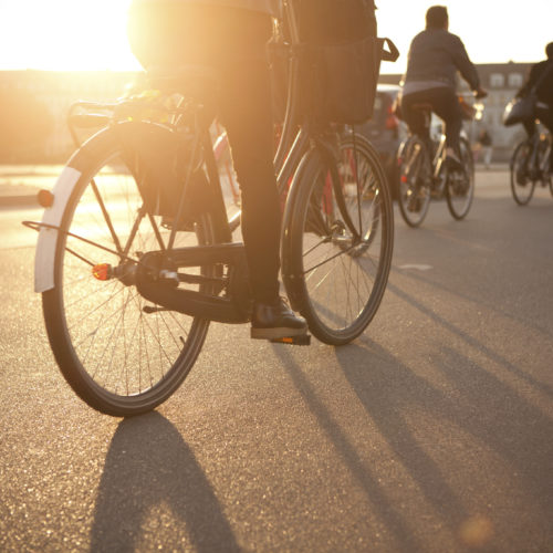 Rückansicht mehrerer Radfahrer, die bei Sonnenuntergang auf der Straße fahren