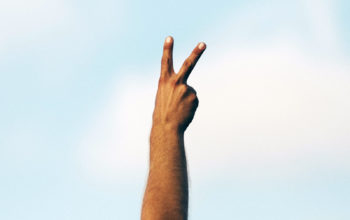 eine Hand fomt mit Zeige- und Mittelfinger das Peace-Zeichen, im Hintergrund ist blauer Himmel