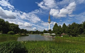 Hamburger Fernsehturm hinter Park und Wasser, vor blauem Himmel