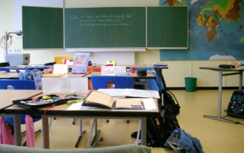 Innenansicht eines Klassenzimmers mit Tischen und einer Tafel im Hintergrund
