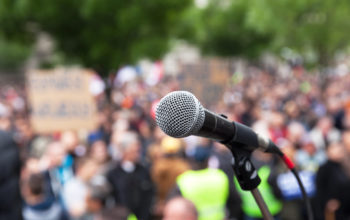 Microphone in focus against blurred crowd. Political rally.