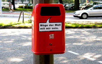 ein roter Mülleimer mit der Aufschrift "Möge der Müll mit mir sein" an einer Straße in Hamburg