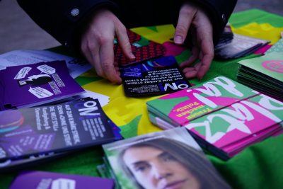 Bild von einem Infostand-Tisch mit (grünen) Flyern zu Feminismus. Ein Flyer, der zum 8.März-Streik aufruft, wird gerade gegriffen.